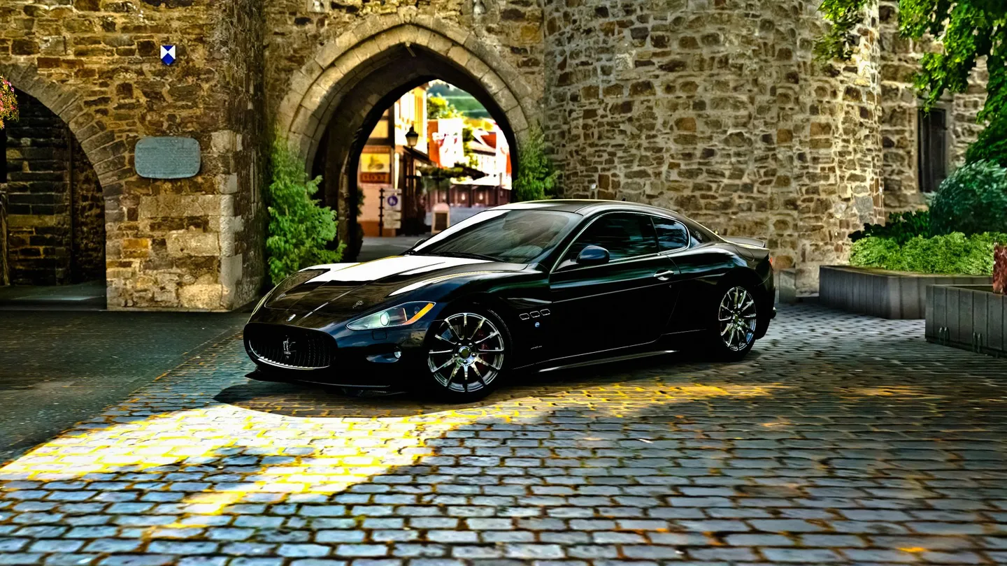 A dark Maserati outside a stone building